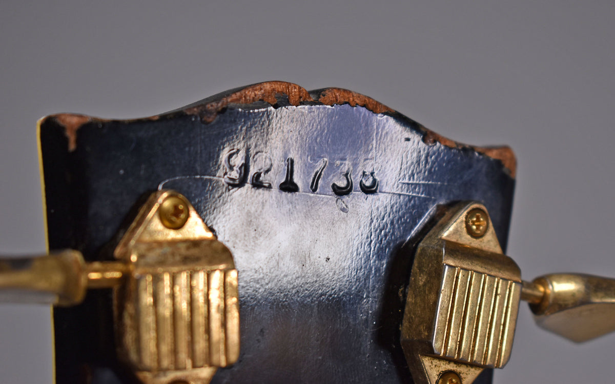 Close-up of the black headstock's top edge, showing serial number 921730, gold tuners, and significant finish wear.