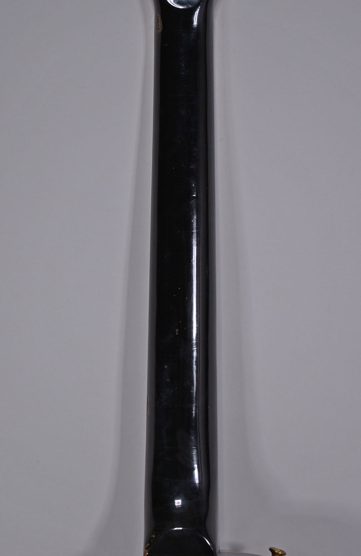 The black gloss neck of the guitar is shown from the back, with visible wear, scratches, and checking along its length.