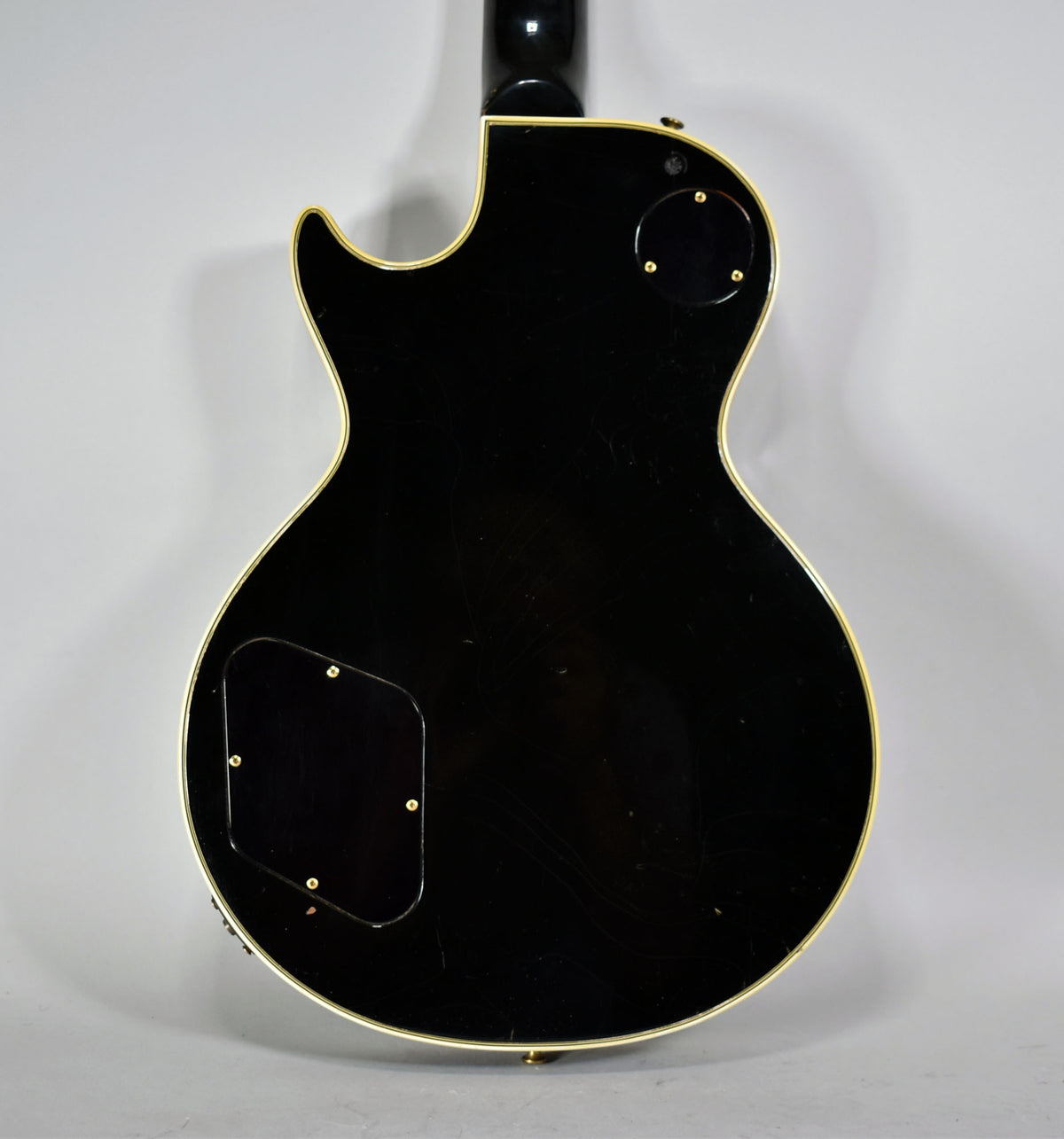 The guitar's glossy black back, framed from the neck joint down, shows light surface scratches and two control cavity covers.