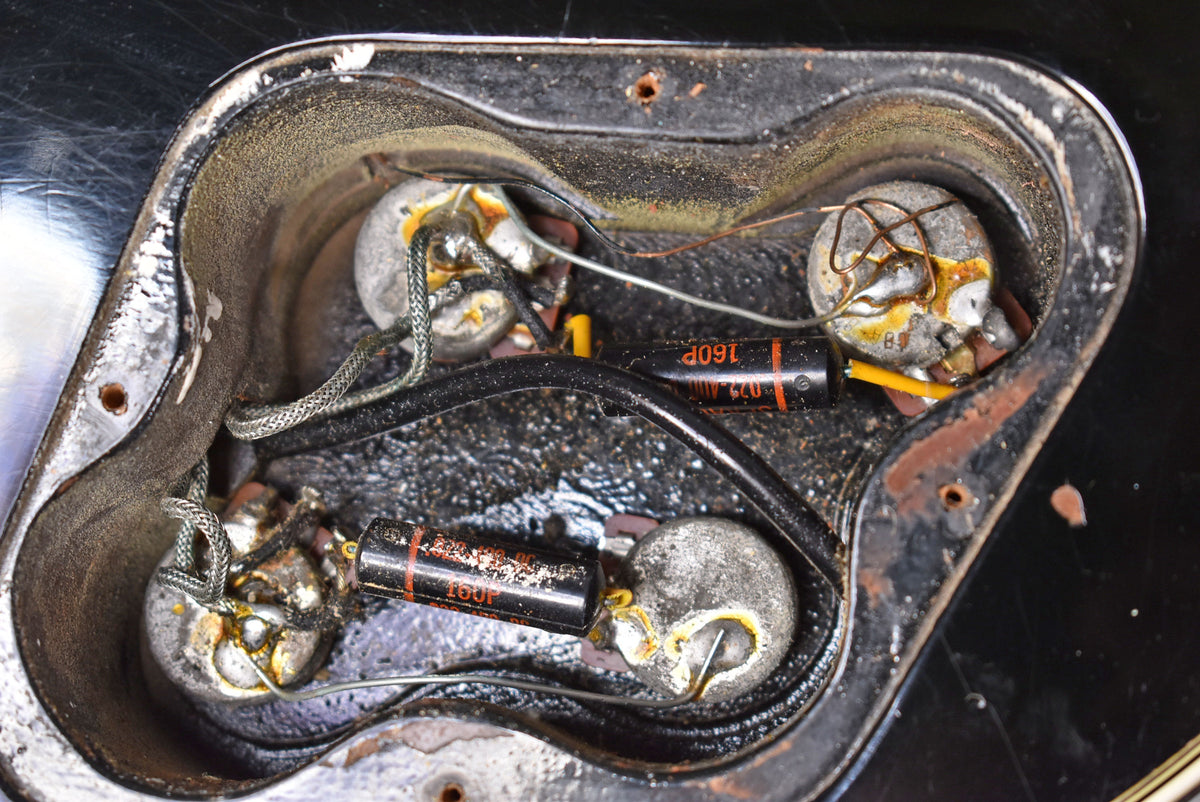 Close-up of the guitar's control cavity, revealing four tarnished potentiometers, two black capacitors, and braided wiring.