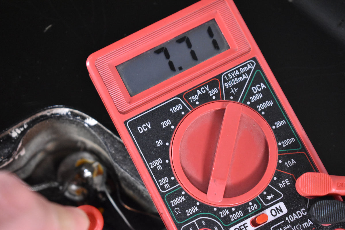 A red multimeter displays "7.71" while testing a capacitor inside the guitar's control cavity, showing worn wiring.
