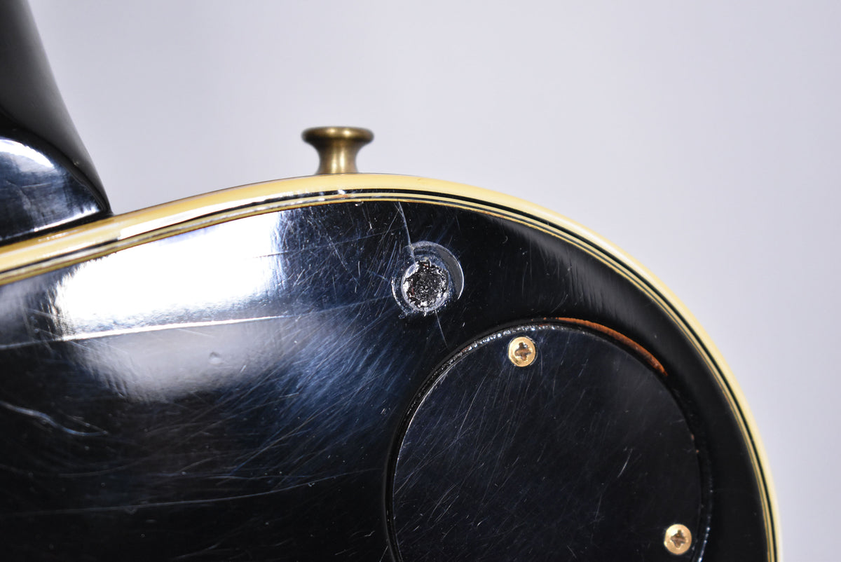 Close-up of the guitar's black body with heavy finish checking, showing a worn strap button hole and a control cavity cover.