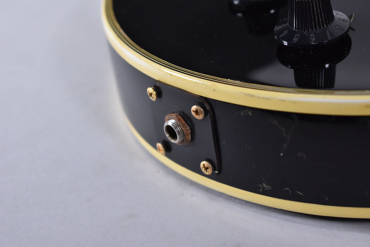 Close-up of the guitar's black body edge, showing the input jack with rust, gold screws, and cream binding with wear.
