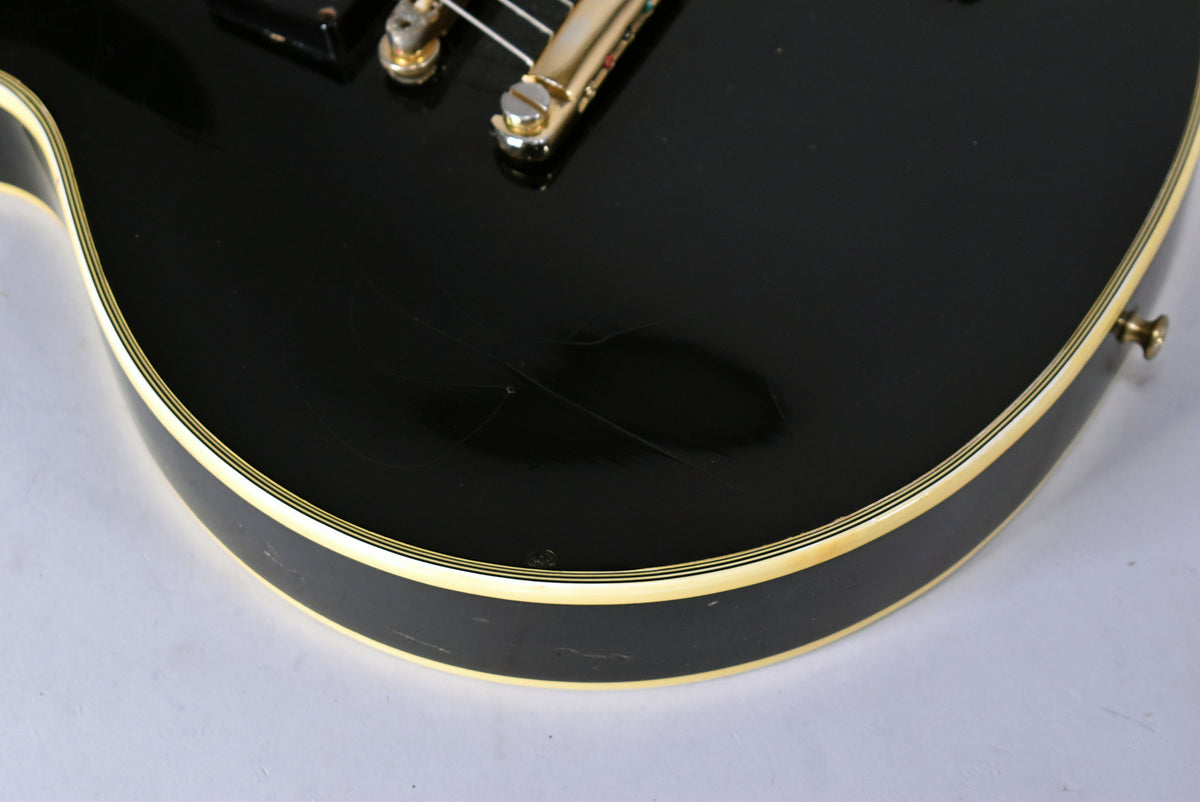 Close-up of the guitar's lower bout, showing the glossy black finish with visible checking and scratches, and cream binding.