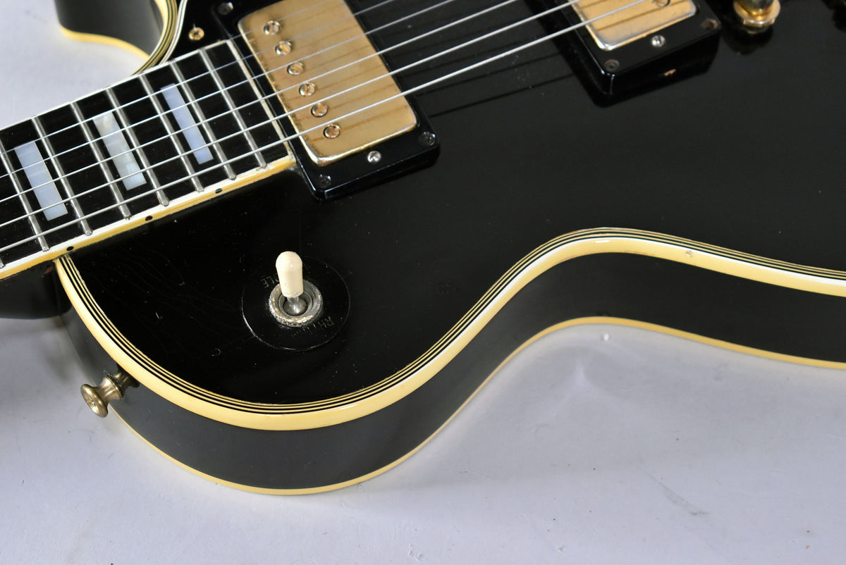 Close-up of the black body with cream binding, showing the pickup selector switch, gold humbucker, and fretboard with block inlays.