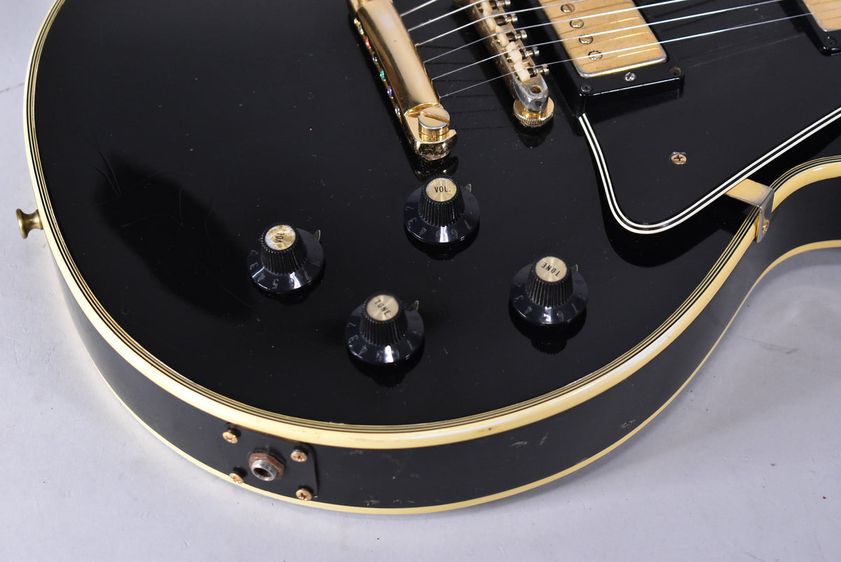Close-up of the black guitar body, showing four black control knobs, gold hardware, and light finish checking and scratches.