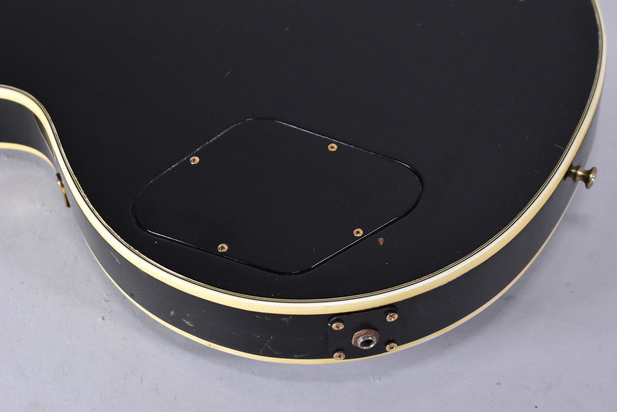 Close-up of the guitar's black back, showing the control cavity cover, output jack, and cream binding with visible wear and checking.