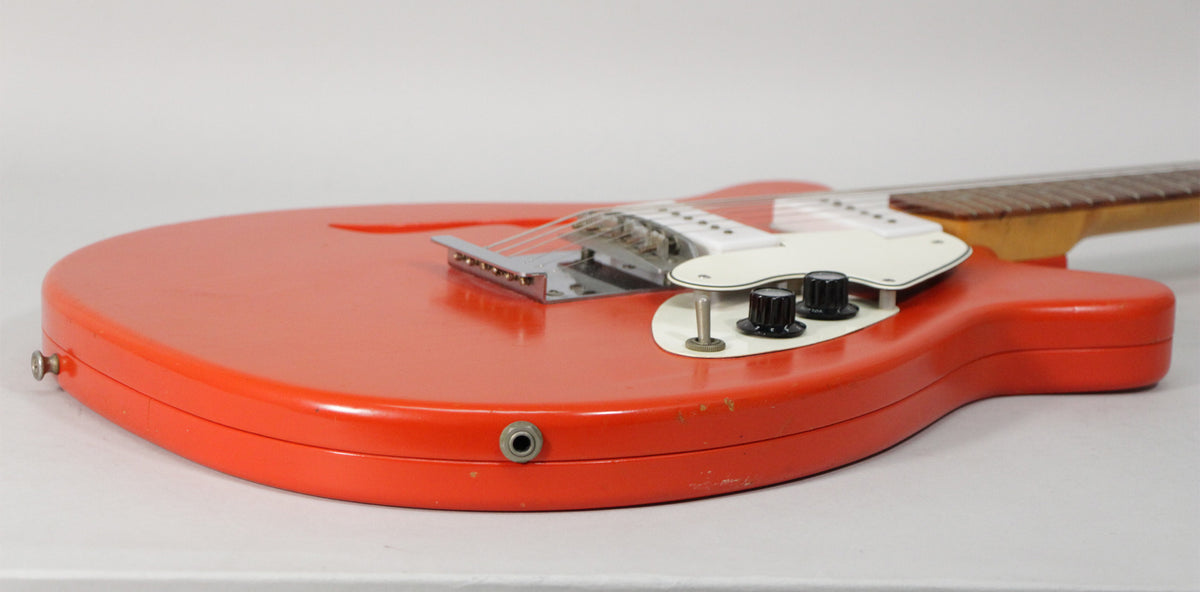 The red electric guitar's lower bout is angled right, showing the input jack, two black knobs, a toggle switch, and some finish wear.
