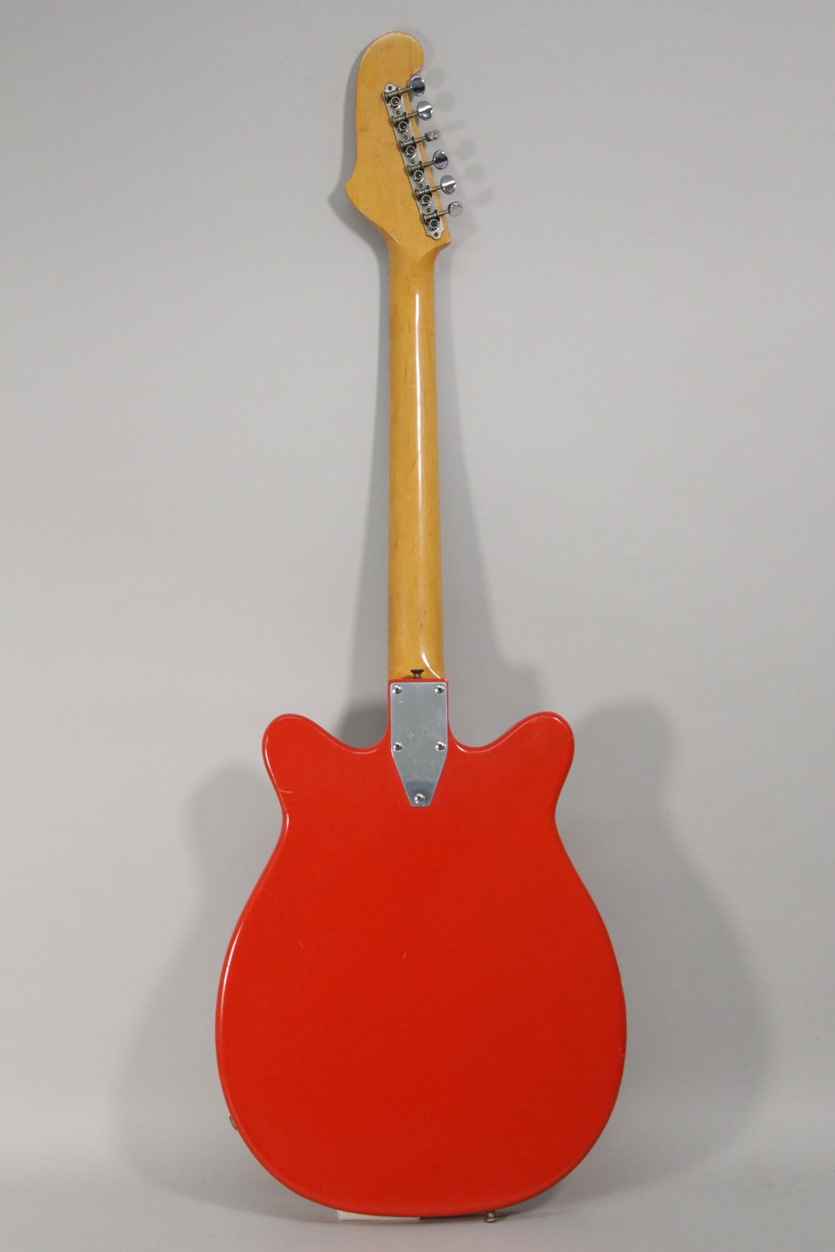 Full rear view of the red electric guitar, showing the maple neck and headstock with six chrome tuners, and a silver neck plate.