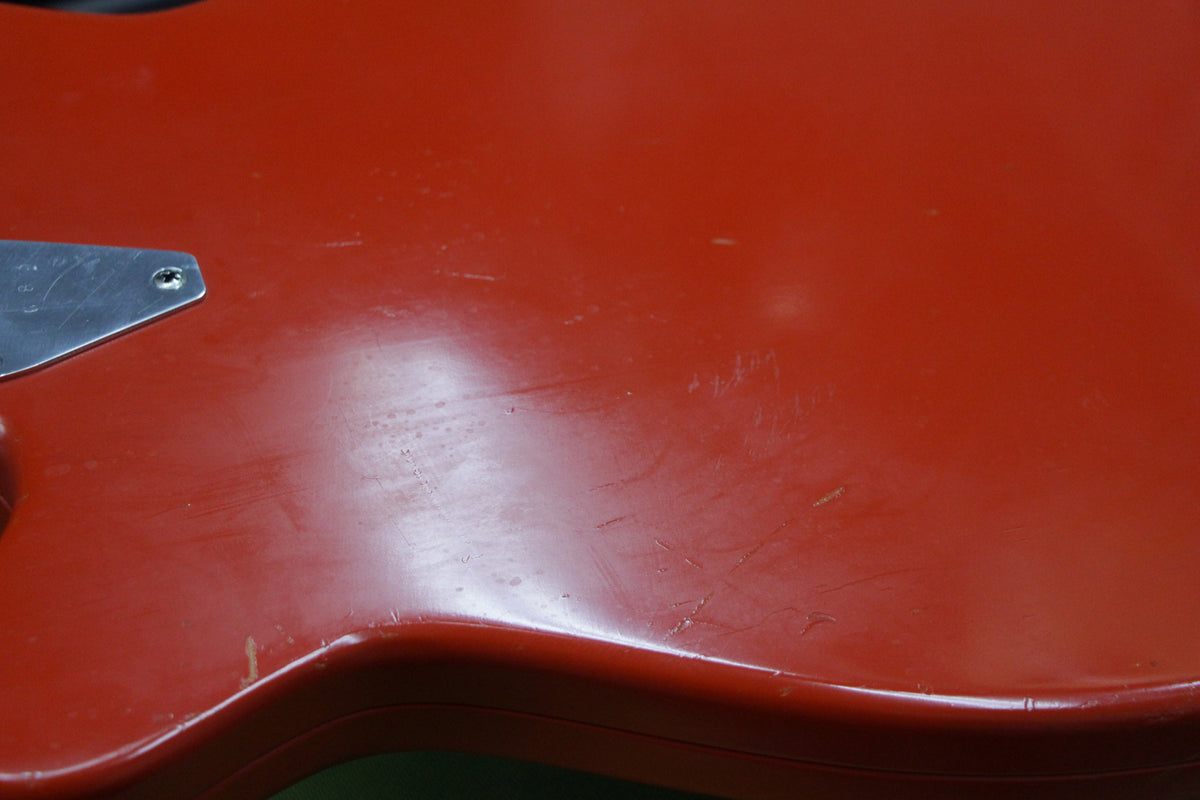 Close-up of the guitar's red body, showing many surface scratches, dings, and a small chip near the lower bout.