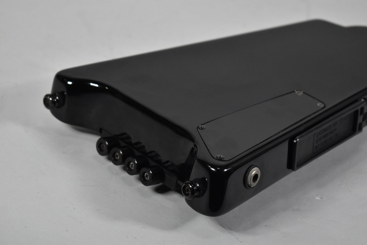 Close-up of the glossy black bass body, showing the four black tuning knobs and output jack on the lower side.