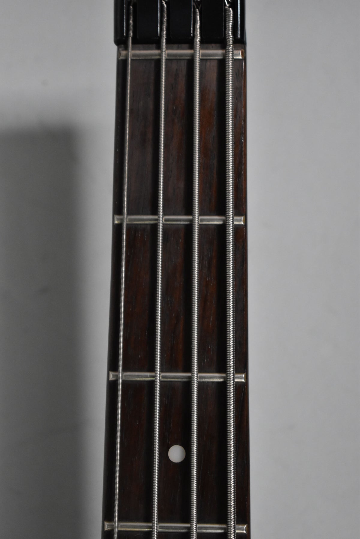 Close-up of the dark rosewood fretboard with four strings, frets, and a single white dot inlay at the 7th fret.