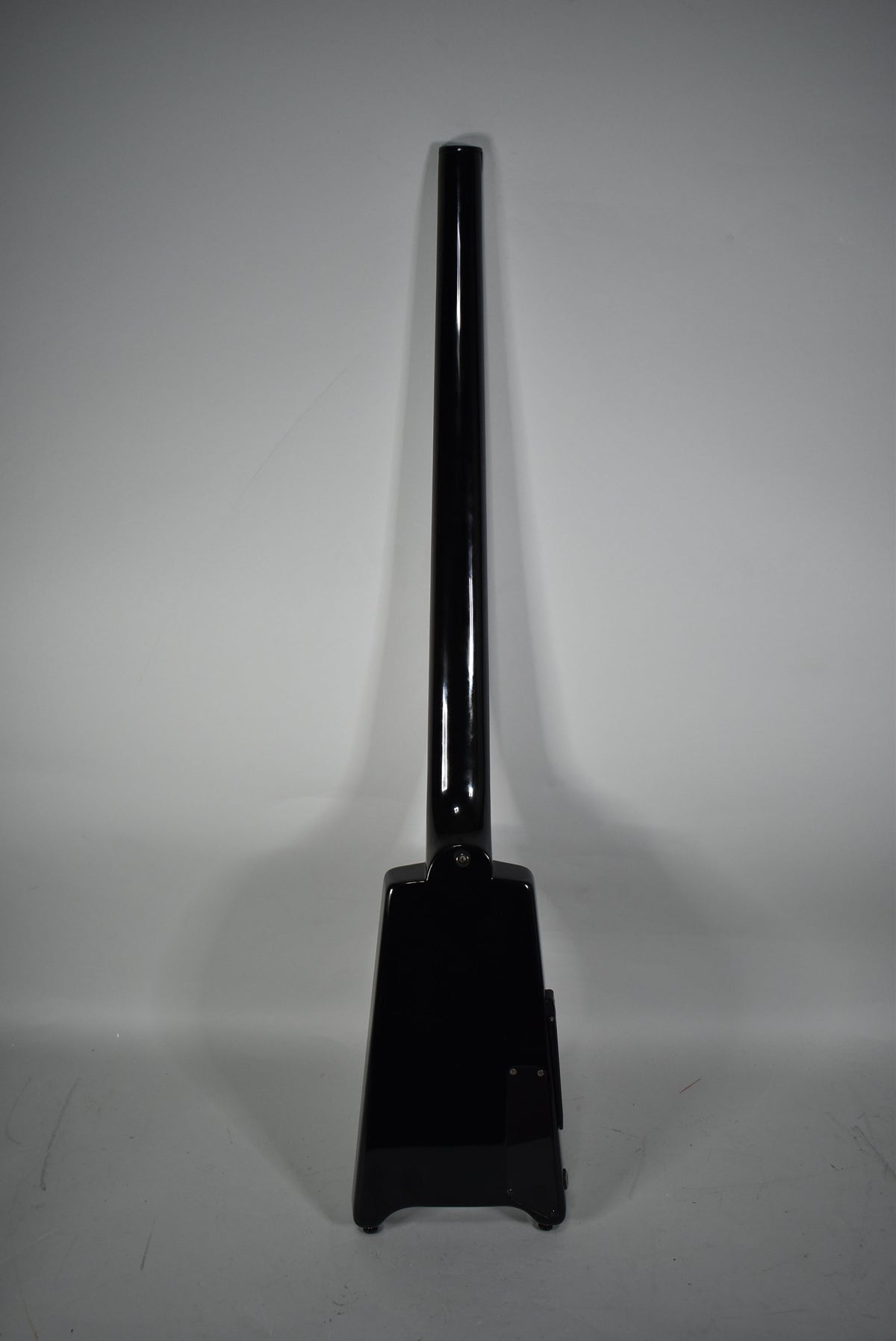 Full rear view of the glossy black headless bass, showing the neck joint and the trapezoidal body with a control cavity cover.