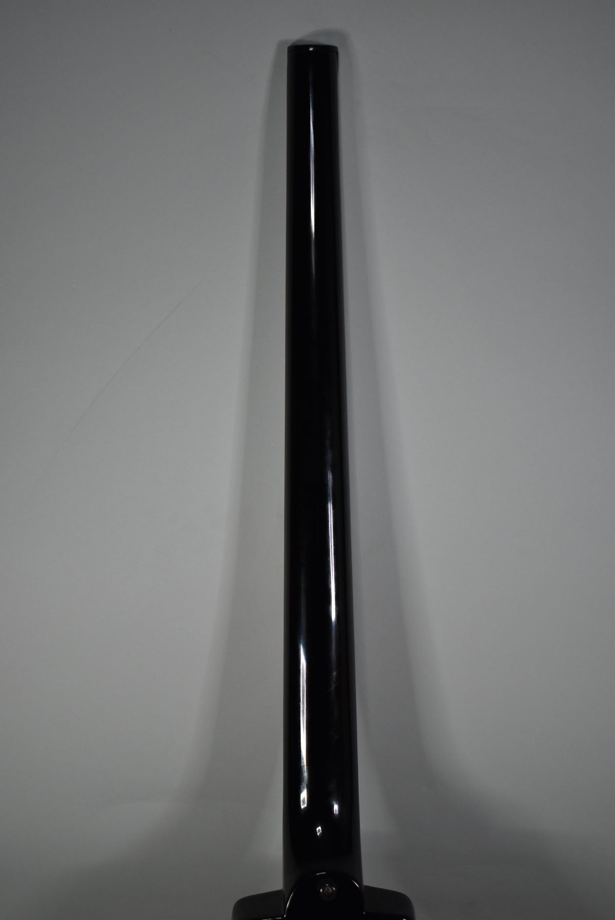 The bass guitar's glossy black neck is viewed from the back, extending vertically with a slight reflection down its center.