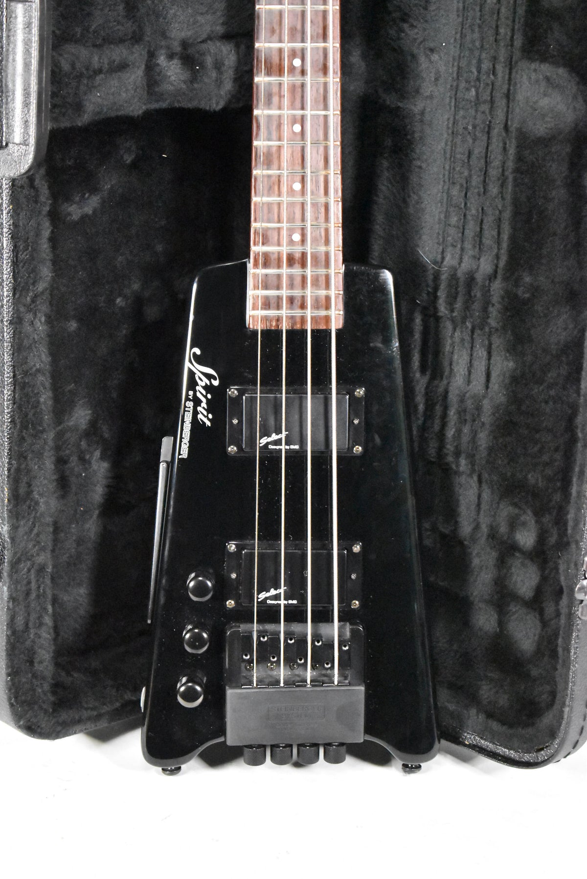 Headless black bass guitar, body and fretboard visible, with two humbucker pickups, three control knobs, and a black hard case.