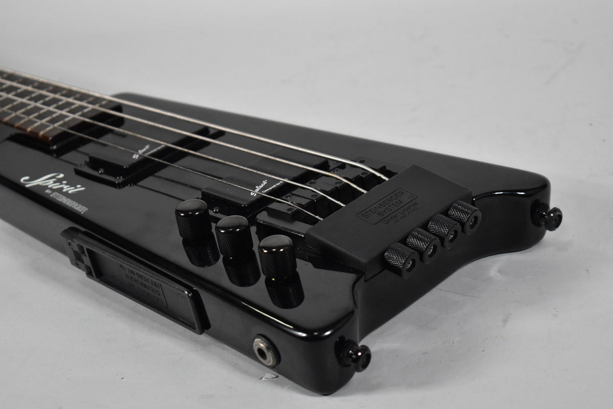 Close-up of the glossy black, headless bass body, showing the bridge, four control knobs, and output jack.