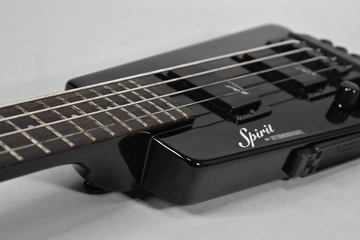 Close-up of the glossy black bass body and fretboard, showing two black pickups, control knobs, and light fret wear.