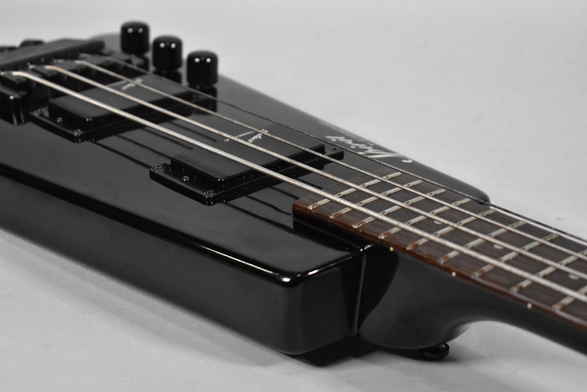 Close-up of the glossy black bass body, showing two humbucker pickups, three control knobs, and the dark fretboard.