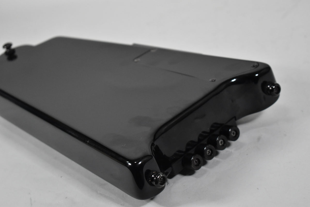 Close-up of the black headless bass guitar's body, showing the four black string tuners and strap buttons on the lower right.