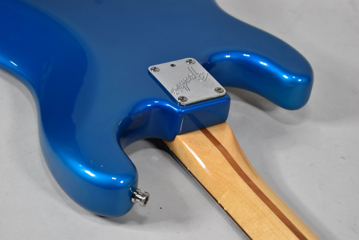 The guitar's glossy blue body meets a light wood neck with a chrome neck plate, showing minor wear near the output jack.