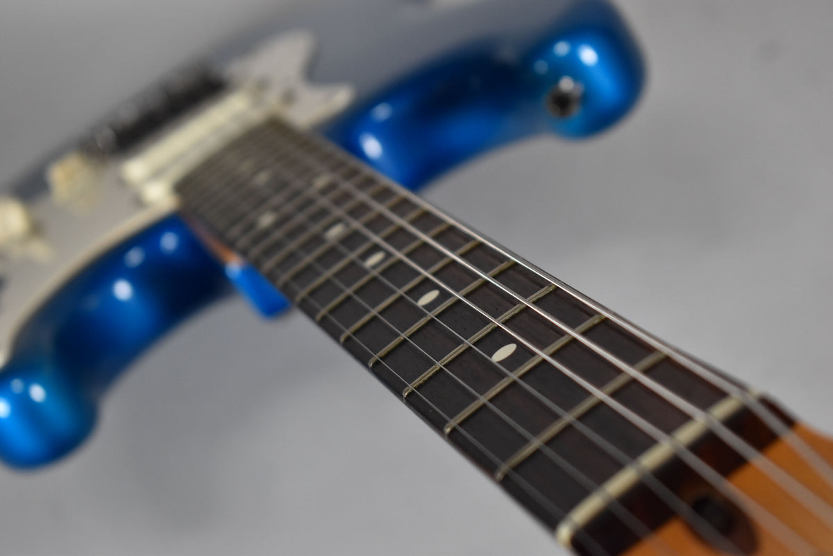 Close-up of the blue Stratocaster's dark fretboard with white dot inlays and light strings, angled from the headstock.