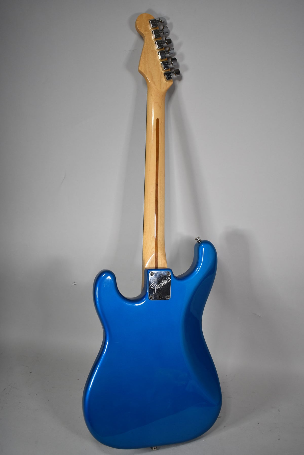 The back of a glossy blue electric guitar, showing the light maple neck, chrome tuners, and neck plate.