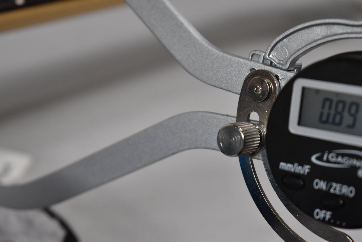A close-up of a digital caliper measuring the guitar's fretboard, displaying "0.89" on its screen.