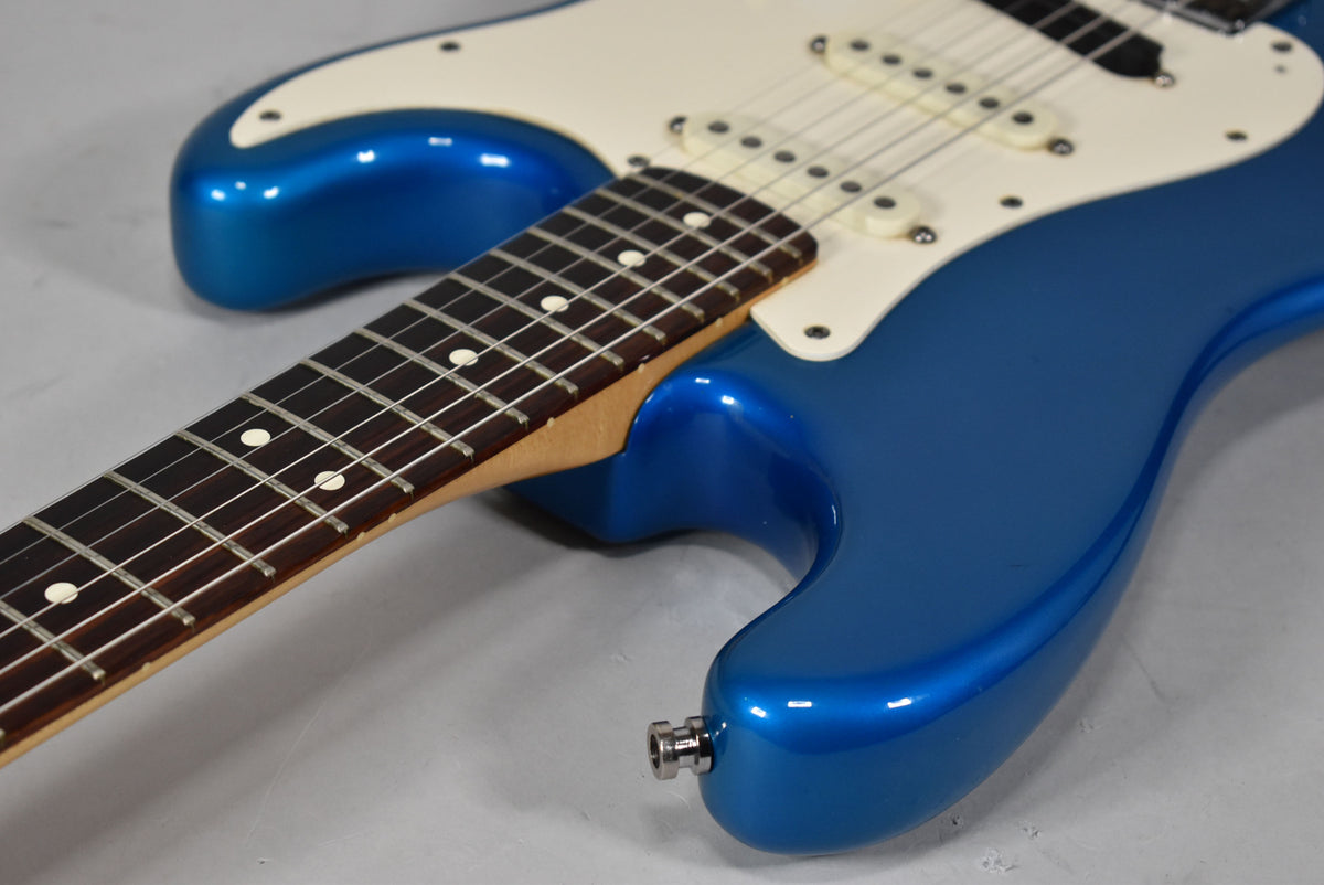 The blue metallic Stratocaster body and neck are angled, showing the white pickguard, three single-coil pickups, and output jack.