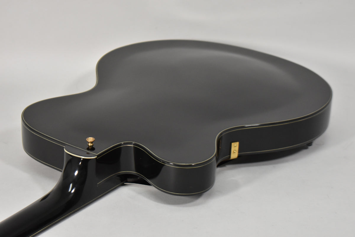 The guitar's black gloss back and sides are visible from the lower bout to the neck heel, with a gold strap button.