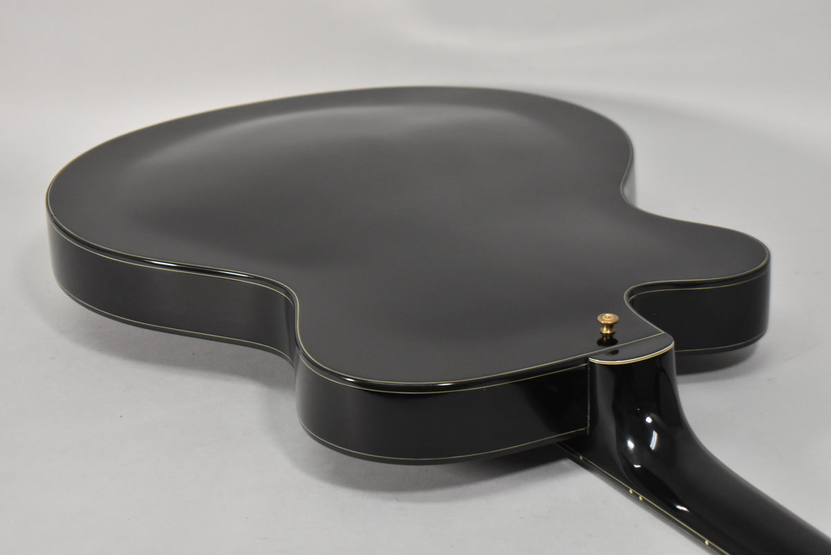 The guitar's black gloss back and sides are visible from the lower bout, with a gold strap button and neck heel.