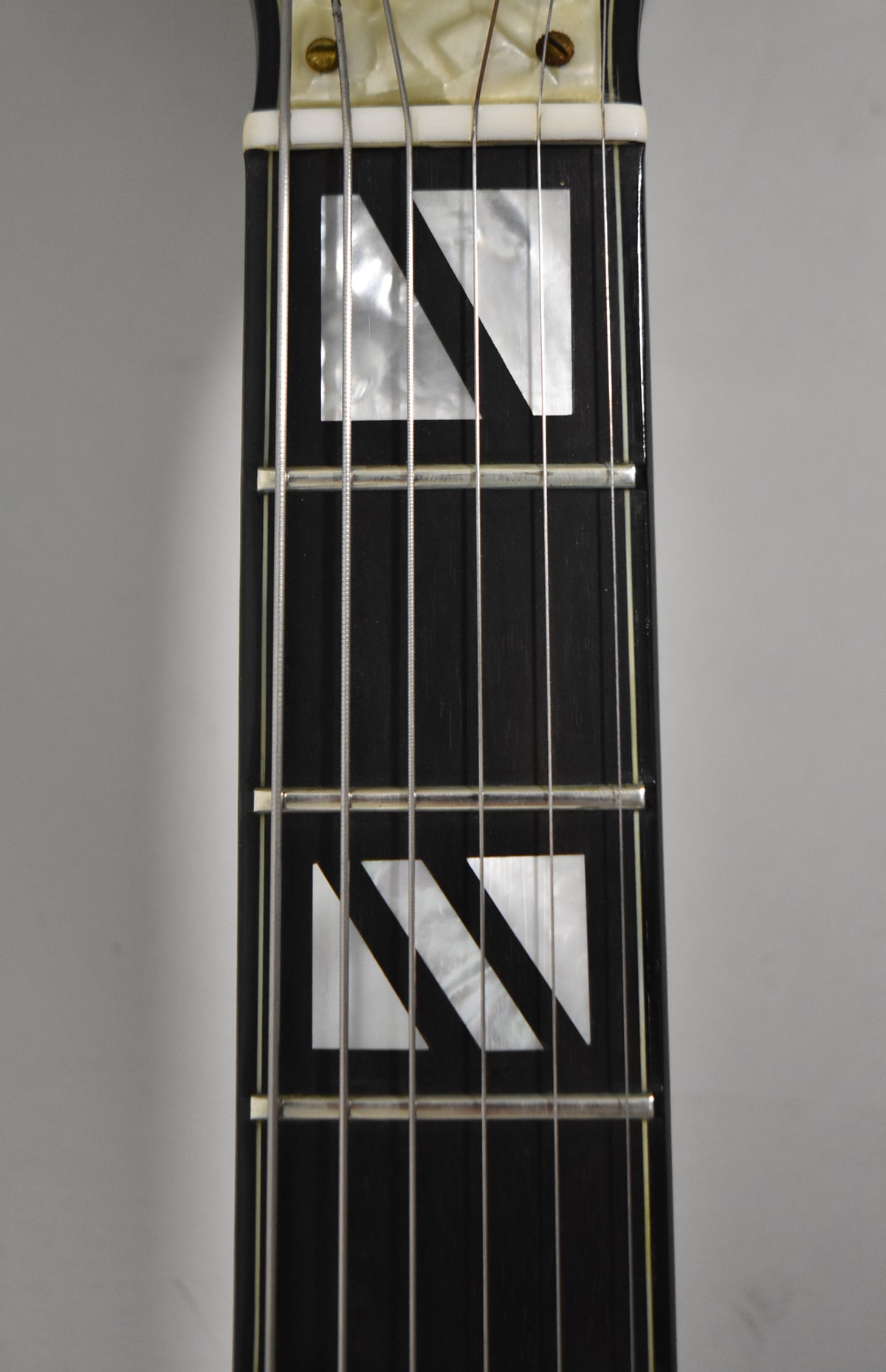 Close-up of the black fretboard with mother-of-pearl block inlays, showing the nut and first three frets.