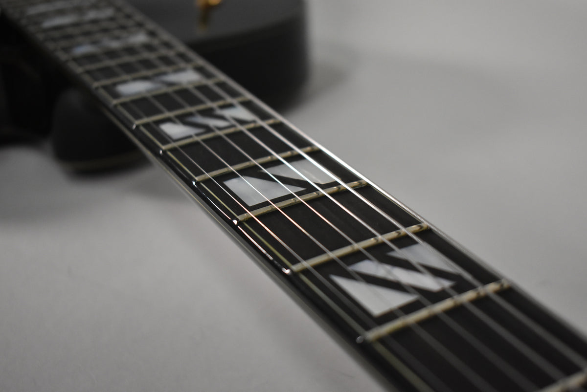 The black guitar's fretboard, with trapezoid mother-of-pearl inlays, is shown at an angle, revealing light fret wear.