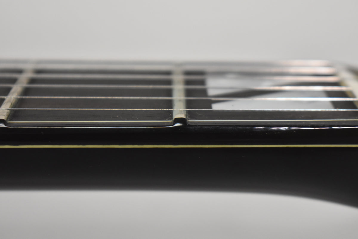 Close-up of the black guitar's fretboard and frets, showing a white binding strip and a thin yellow line along the side.