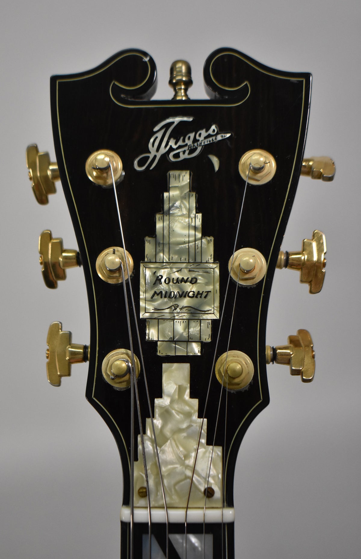 Close-up of the black headstock with gold tuners and an ornate mother-of-pearl inlay, showing some light wear.