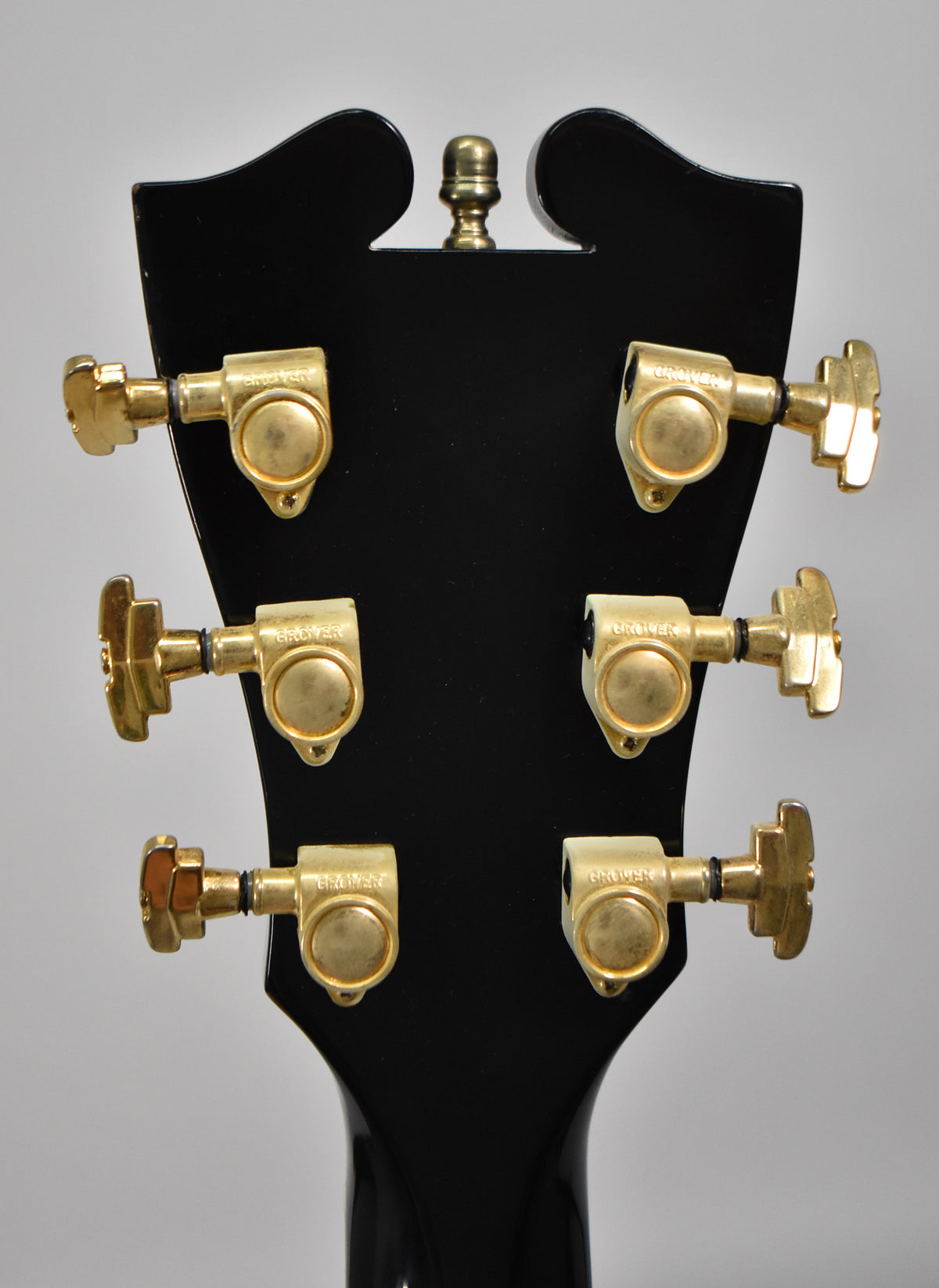 The back of a black guitar headstock with six gold Grover tuners, three on each side, and a gold string tree at the top.