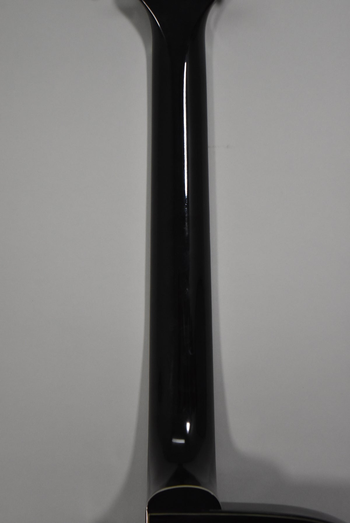 The guitar's glossy black neck, with visible wear and light scratches, extends from the body, which has cream binding.