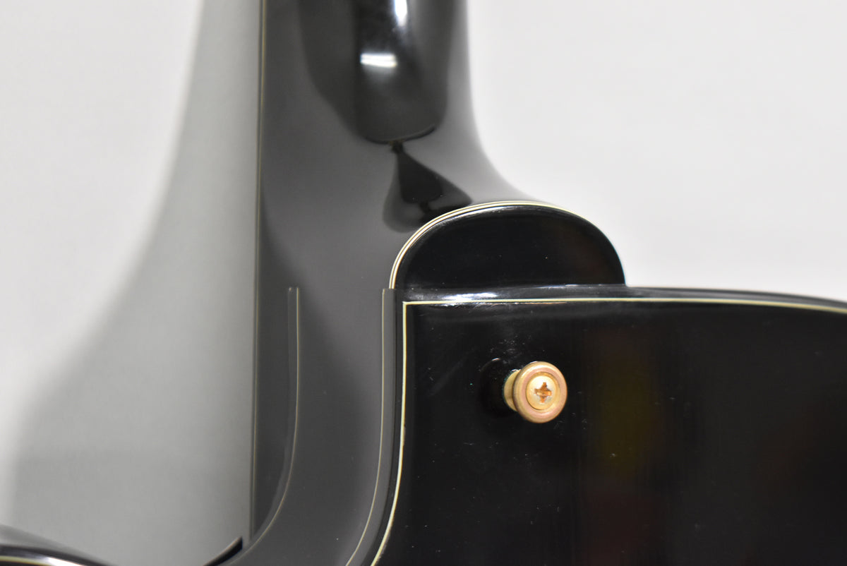 Close-up of the guitar's black gloss body and neck heel, showing a gold strap button and light wear on the finish.