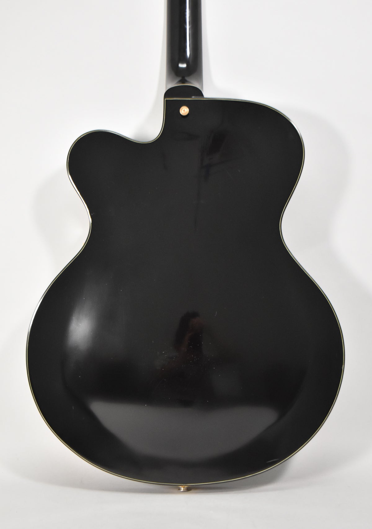 The full back of the black archtop guitar is shown, revealing a glossy finish with light scratches and a gold strap button.
