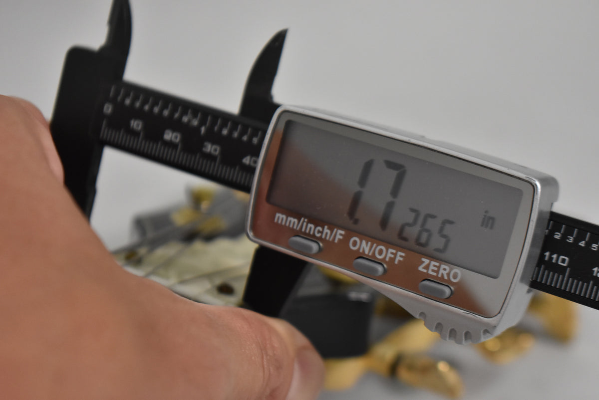 A digital caliper measures the guitar's nut width at 1.7265 inches, held by a hand over the black finish.