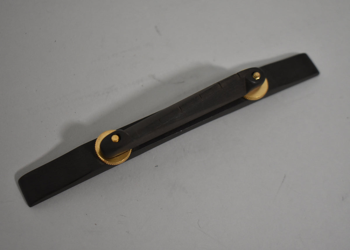 A dark brown wooden bridge with two brass-colored adjustment wheels, angled on a light gray surface.