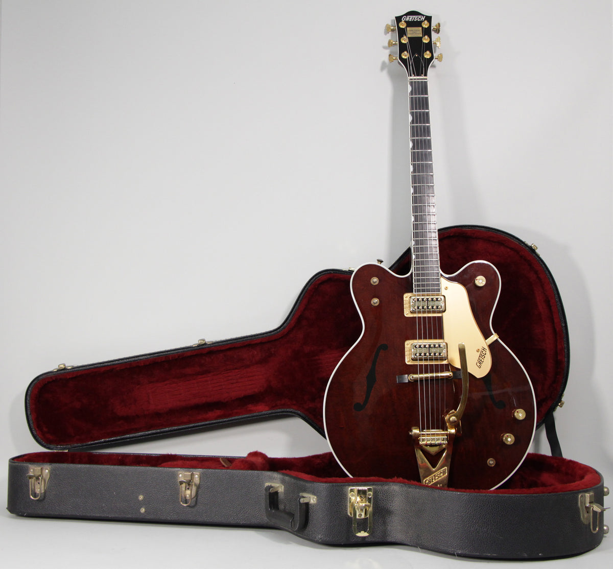 Full-length view of a dark cherry red hollow body guitar with gold hardware, standing in its open black hard case with red plush lining.