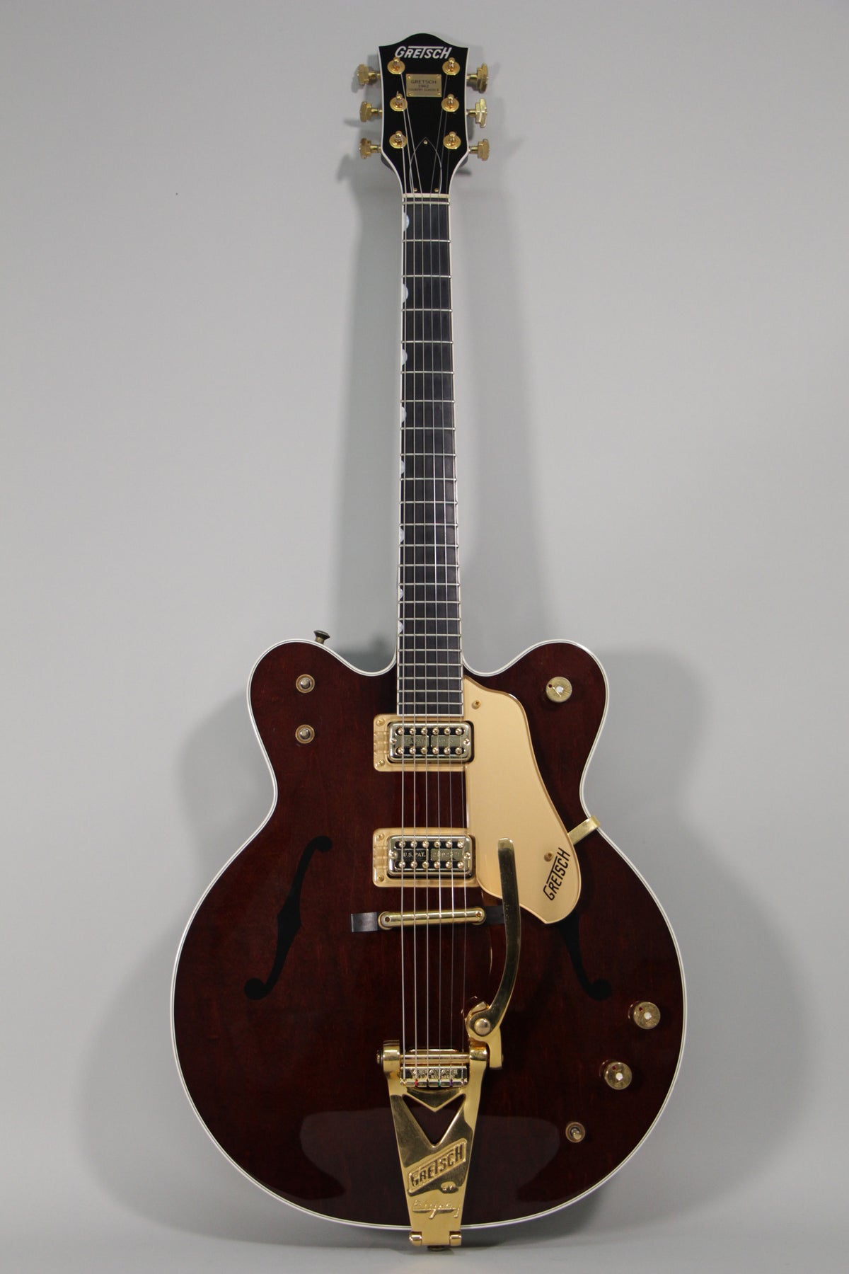 Full front view of a dark cherry hollow body guitar with gold hardware, f-holes, and a gold Bigsby vibrato tailpiece.