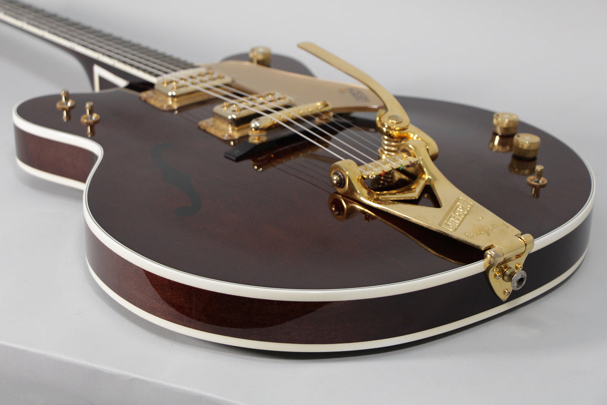 Close-up of a dark brown hollow-body guitar with gold hardware, showing the Bigsby vibrato, pickups, and F-hole.