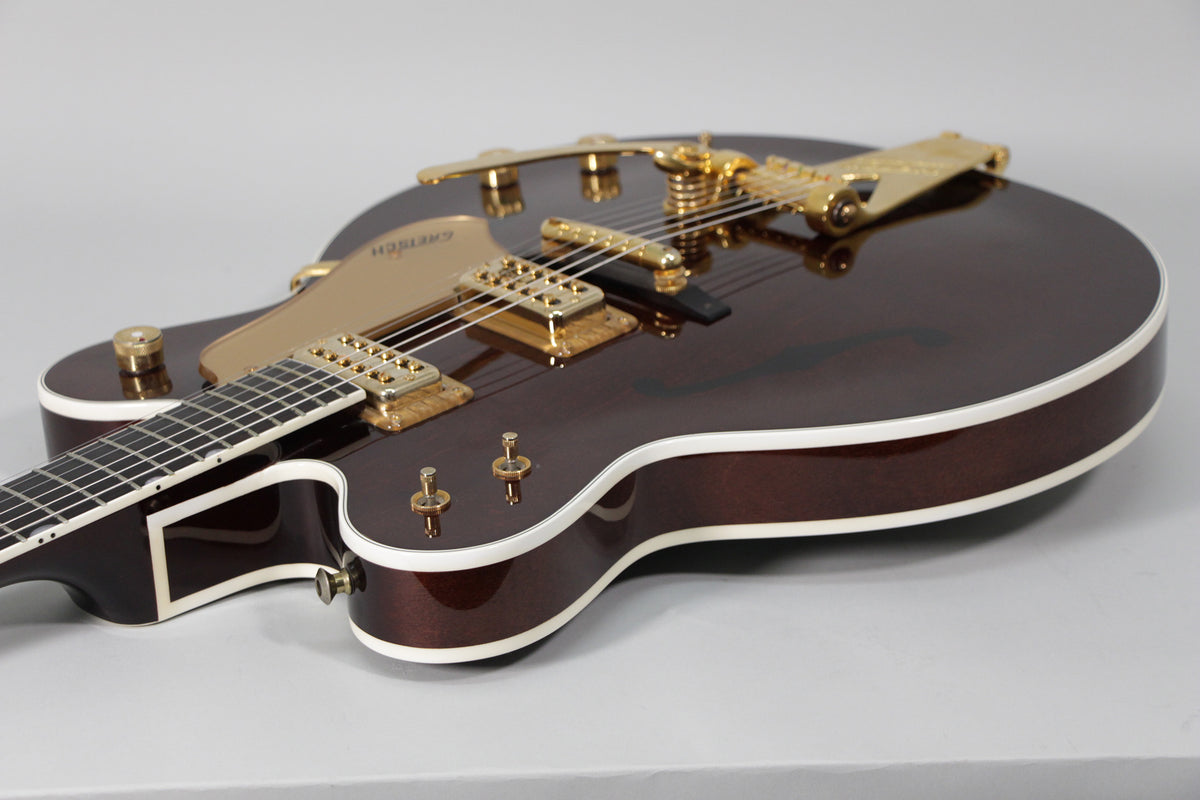 The dark brown hollow body guitar, with white binding, gold hardware, and f-holes, is angled from the lower bout.