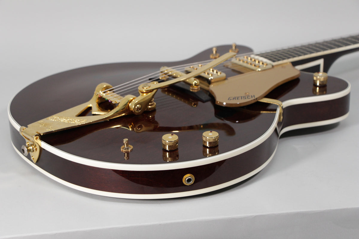 The dark brown hollow body guitar, with white binding, is angled from the lower bout, showing the gold Bigsby and pickup.