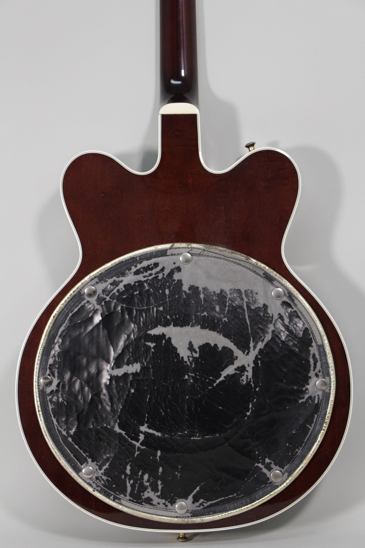 The guitar's dark cherry back, with white binding, shows a large, worn black and silver circular pad.