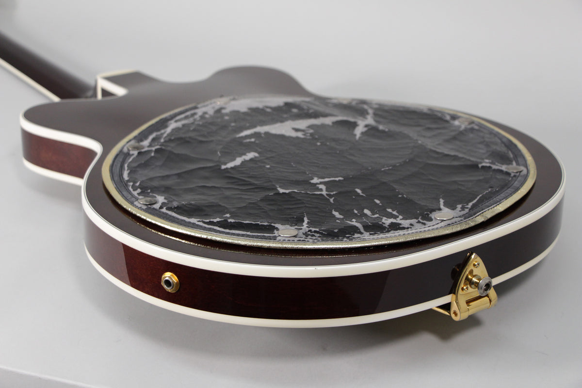 The guitar's dark cherry back and side, with cream binding, shows a worn black back pad and gold strap button.