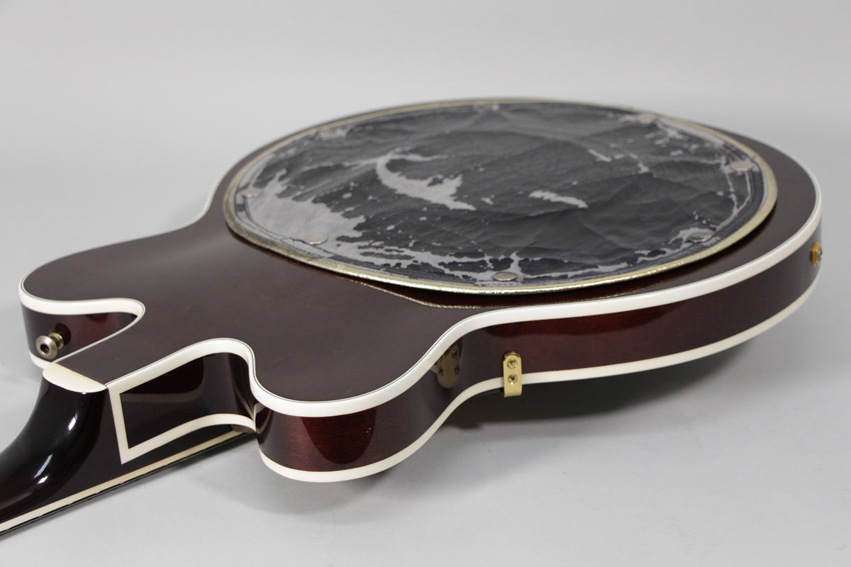 Upper bout of a dark cherry red guitar, showing the pickguard with heavy wear and a gold strap button.