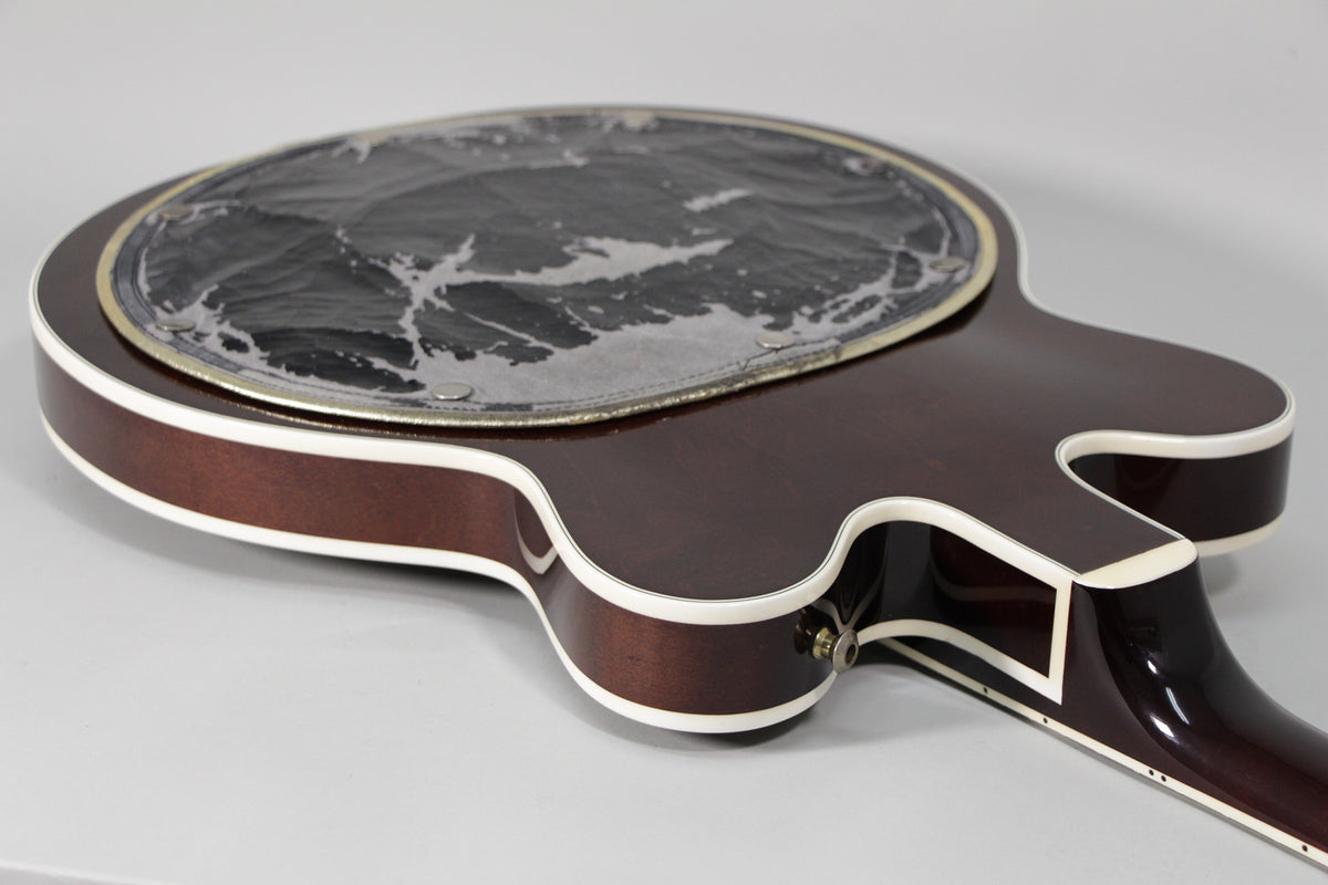 The dark brown guitar body, with white binding, shows a large, round, heavily worn black and silver pickguard.