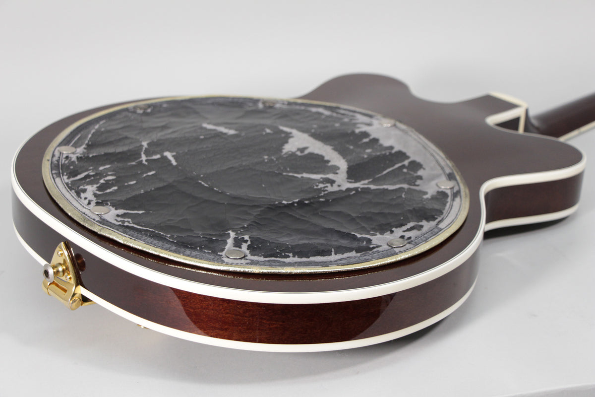 The guitar's dark cherry back shows a worn, peeling black leather pad, with a gold strap button on the lower bout.